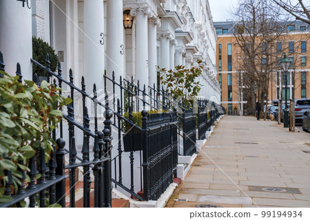 Empty sidewalk and row of beautiful white Edwardian houses with metallic railing and columns in Kensington, London 99194934