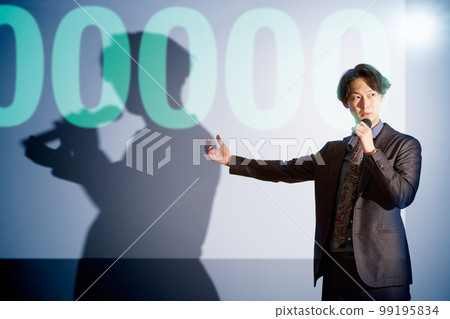 A young business person giving a speech with a microphone on the background of a slide A young business person giving a speech with a microphone on the background of a slide 99195834