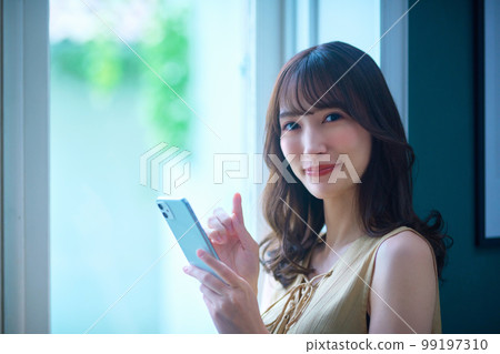 Beauty image of a young woman operating a smartphone by the window Beauty image of a young woman operating a smartphone by the window 99197310