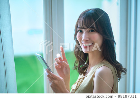 Beauty image of a young woman operating a smartphone by the window Beauty image of a young woman operating a smartphone by the window 99197311