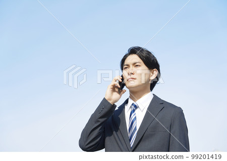 Businessman making a phone call on a smartphone outside Blue sky background 99201419