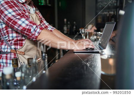 cropped shot of young barista taking notes and using laptop. cropped shot of young barista taking notes and using laptop. 99201850