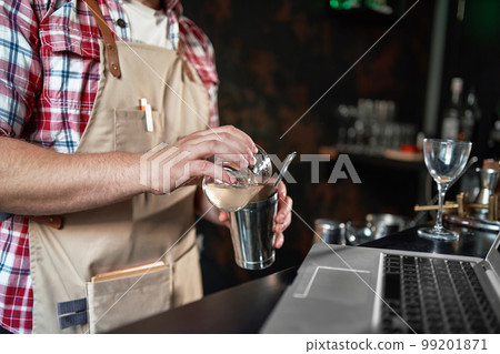 bartender pouring a cocktail from a shaker into a glass. 99201871