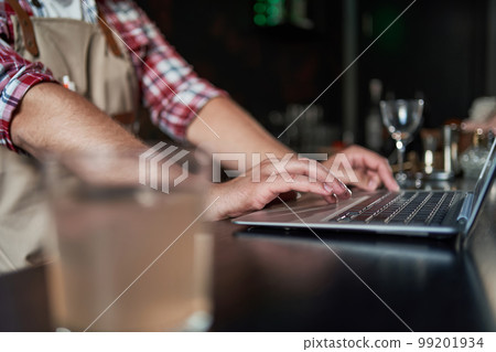 cropped shot of young barista taking notes and using laptop. cropped shot of young barista taking notes and using laptop. 99201934