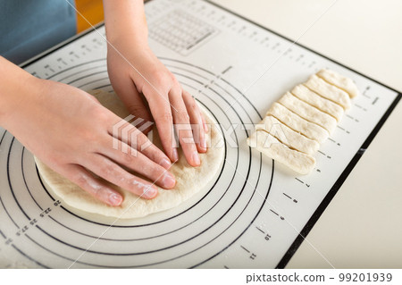 Close-up of hands kneading rolled out dough on a kitchen baking mat with round markings of different diameters 99201939