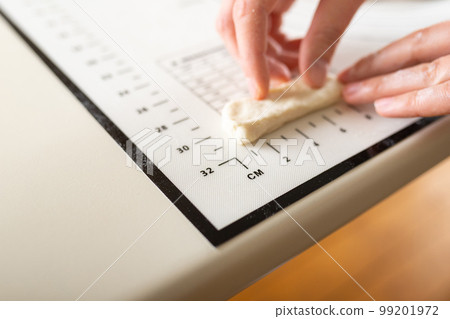 Close-up of hands measuring the length of a piece of dough on a kitchen mat with metric markings. Copy space 99201972