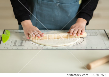 Rolling out the dough with a wooden rolling pin on a silicone baking mat. View of hands and workspace. copy space 99201975