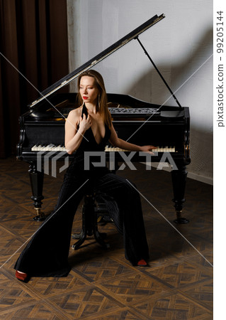 Pretty woman in dress jumpsuit sitting near grand piano 99205144