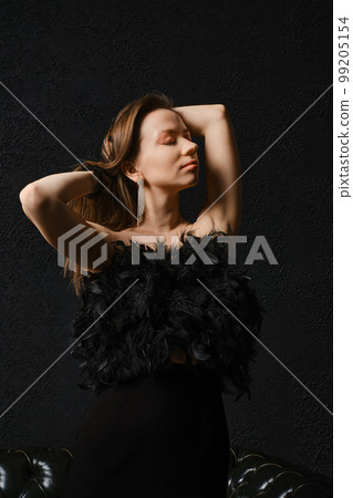 Stylish woman in corset with feathers with closed eyes over black background 99205154