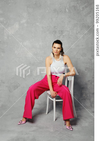 A woman in wide magenta trousers sits on chair with her legs spread wide A woman in wide magenta trousers sits on chair with her legs spread wide 99205168