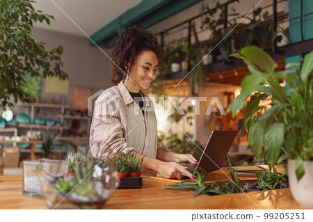 Smiling female florist working online from own floral studio and check customers order  99205251