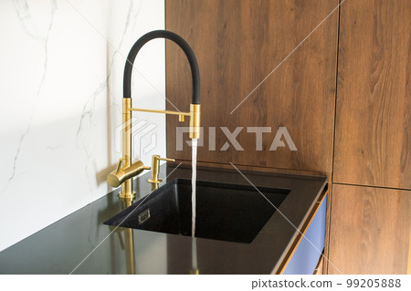Water pours from the black and gold faucet in the kitchen into the sink 99205888