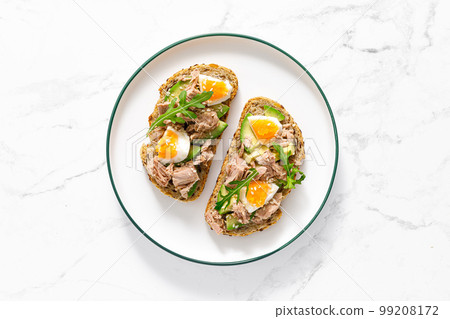 Tuna toast. Open sandwiches with whole grain bread, canned tuna, boiled egg, avocado and arugula. Top view Tuna toast. Open sandwiches with whole grain bread, canned tuna, boiled egg, avocado and arugula. Top view 99208172