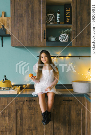 Portrait of a cheerful little girl with tangerines in her hands in the Christmas kitchen, cozy home 99209011