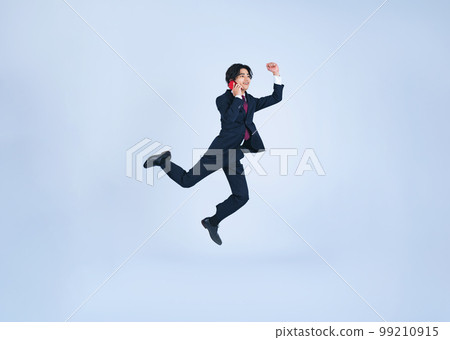 A young businessman jumping while talking on his smartphone (Cutout PNGs are also available for sale! See author profile) 99210915