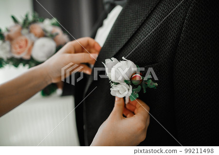 Beautiful bride putting on boutonniere with roses on groom suit 99211498