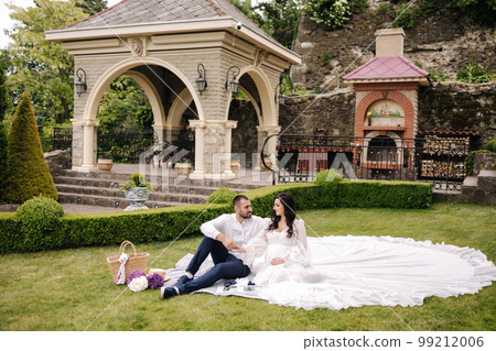 Beautiful couple sitting on a plaid on the grass. Elegant pregnant woman with husband waiting for baby. Future parents Beautiful couple sitting on a plaid on the grass. Elegant pregnant woman with husband waiting for baby. Future parents 99212006