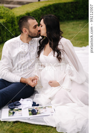 Portrait of beautiful couple sitting on a plaid on the grass. Elegant pregnant woman with husband waiting for baby. Future parents Portrait of beautiful couple sitting on a plaid on the grass. Elegant pregnant woman with husband waiting for baby. Future parents 99212007