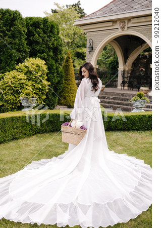 Elegant pregnant woman in beautiful white dress walking outdoors. Future mom hold wicker basket with flowers Elegant pregnant woman in beautiful white dress walking outdoors. Future mom hold wicker basket with flowers 99212040
