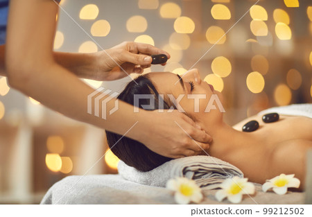 Beautiful young woman getting massage at a spa salon with stones. 99212502