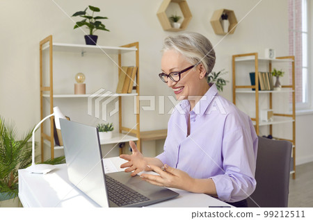 Friendly senior business woman is holding online webinar via video link in her office. 99212511