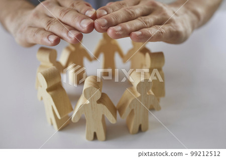 Insurance agent's hands protect wooden figures of people standing in circle in front of him. Insurance agent's hands protect wooden figures of people standing in circle in front of him. 99212512