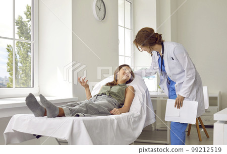 Young patient girl lying on couch during medical examination in clinic and talking with a doctor. 99212519