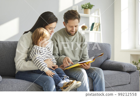 Parents and their adorable toddler baby reading book 99212558
