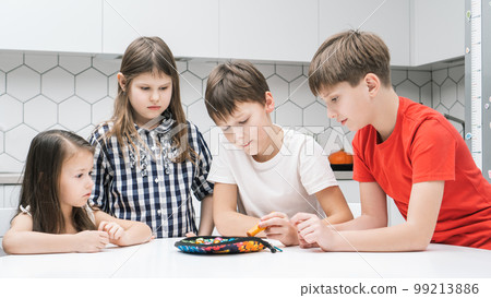 Group of friends play toy fishing on kitchen table. Smart boy hold fishing rod and pick up playthings from plate. 99213886