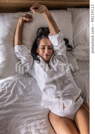 A young woman wakes up in her bedroom bed, stretches her arms and shoulders A young woman wakes up in her bedroom bed, stretches her arms and shoulders 99214113