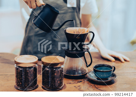 A young female clerk pouring drip coffee in a coffee kettle Faceless A young female clerk pouring drip coffee in a coffee kettle Faceless 99214417
