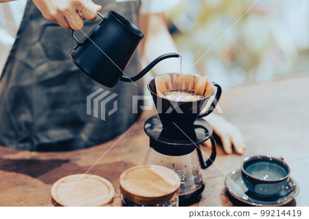 一位年輕的女店員在咖啡壺裡倒滴漏咖啡 一位年輕的女店員在咖啡壺裡倒滴漏咖啡 99214419