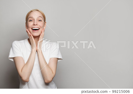 Happy smiling surprised blond woman posing against grey studio wall background 99215006