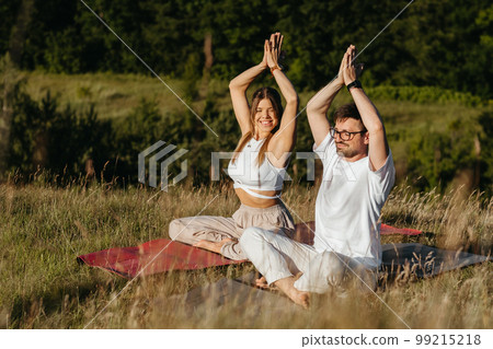 Cheerful Woman and Happy Man Raising Hands Up Over Heads, Young Adult Couple Meditating Outdoors in the Nature 99215218