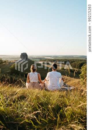 Man and Woman Practicing Yoga and Meditation Outdoors at Sunset with Scenic Landscape and Nature Miracle Giant Stone on the Background Man and Woman Practicing Yoga and Meditation Outdoors at Sunset with Scenic Landscape and Nature Miracle Giant Stone on the Background 99215263