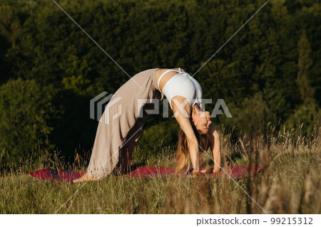 Young Woman Doing Bridge Exercise During Yoga Practice Outdoors with Beautiful Background Young Woman Doing Bridge Exercise During Yoga Practice Outdoors with Beautiful Background 99215312