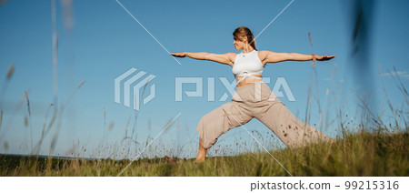 Young Woman Practicing Yoga Outdoors in the Field with Blue Sky on the Background Young Woman Practicing Yoga Outdoors in the Field with Blue Sky on the Background 99215316