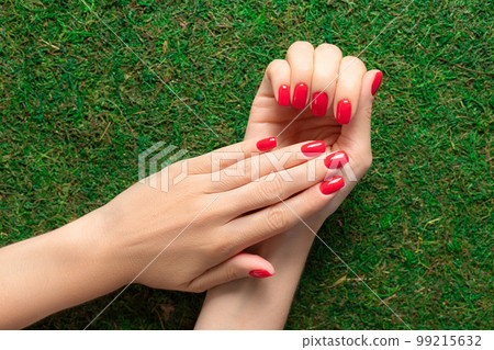 Beautiful female hands with red nail design on green grass background. beauty salon concept. top view 99215632