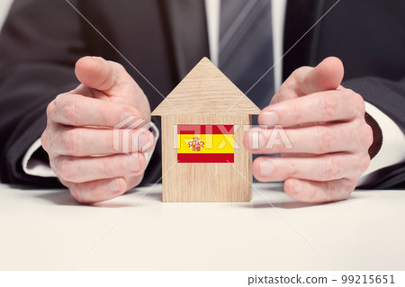 Businessman hand holding wooden home model with Spanish flag. insurance and property concepts 99215651