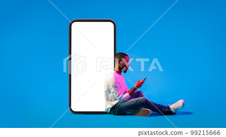 Relaxed black guy sitting by big cell phone on blue 99215666