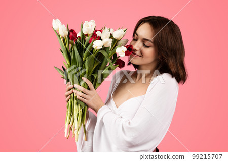 Glad young european woman smelling bouquet of flowers, enjoy lifestyle and aroma of tulips 99215707