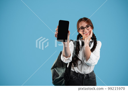 Smiling caucasian teenage girl with pigtails in glasses, student shows smartphone with blank screen 99215970