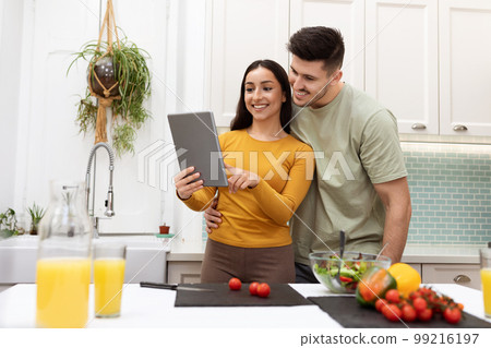 Cheerful hispanic couple looking for recipe on Internet, using pad 99216197