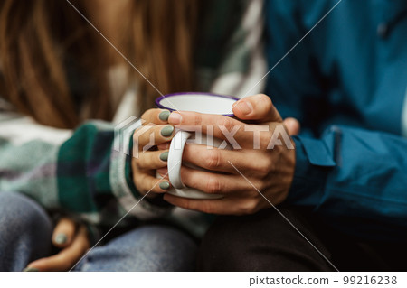 Hands of millennial caucasian woman and guy in jackets hold cup of hot drink, travel in cold forest 99216238