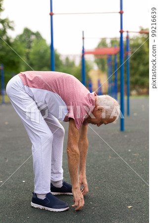 Grandfather jogger doing stretching outdoors before running in summer park 99216639