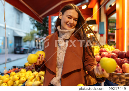 Good looking young woman standing in front of fruit shelves buying groceries in the street Good looking young woman standing in front of fruit shelves buying groceries in the street 99217449
