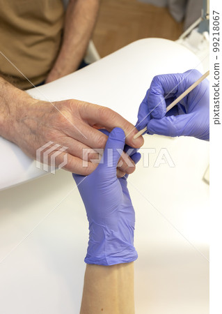 Man's hands on work station in manicure beauty salon. Nail professional doing mature male's nail treatment in spa, pushing cuticle back with orange stick. Safe eco Japanese manicure. Vertical plane Man's hands on work station in manicure beauty salon. Nail professional doing mature male's nail treatment in spa, pushing cuticle back with orange stick. Safe eco Japanese manicure. Vertical plane 99218067