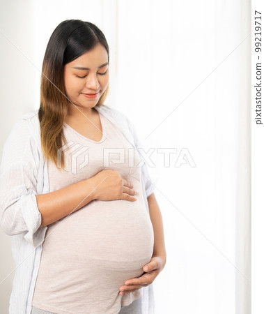 pregnant woman standing near window at home pregnant woman standing near window at home 99219717