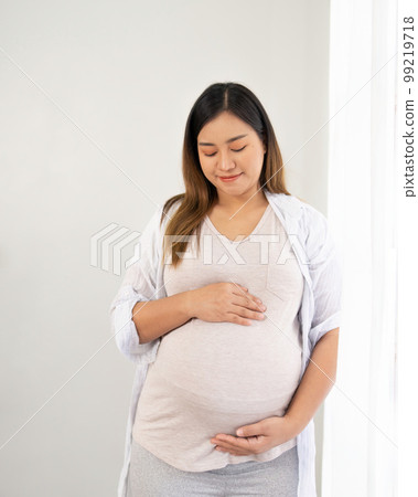 pregnant woman standing near window at home pregnant woman standing near window at home 99219718
