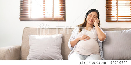 Happy Asian pregnant woman listening to music through her headphones on sofa. pregnancy lifestyle Happy Asian pregnant woman listening to music through her headphones on sofa. pregnancy lifestyle 99219721